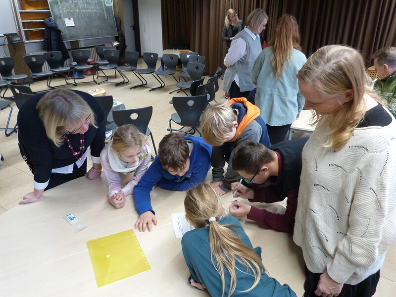 Auf dem Foto sieht man von links Vizelandrätin Silke Engler und rechts Schulleiterin Michaela Krumme zusammen mit Schülern/innen der 4a der Grundschule Niedervellmar beim Rätsel lösen.