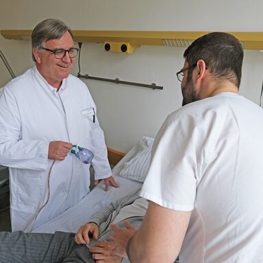 Prof. Dr. Jürgen Fass gemeinsam mit Pfleger Abdo am Patientenbett des Bauchspeicheldrüsenpatienten.
